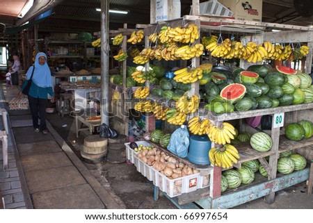 LABUAN - JULY 16: A shopper walks to a fruit stall at the Labuan wet market. July 16, 2010 Labuan, Borneo.  Fresh fruits and farm produce are easily available in this traditional wet market.