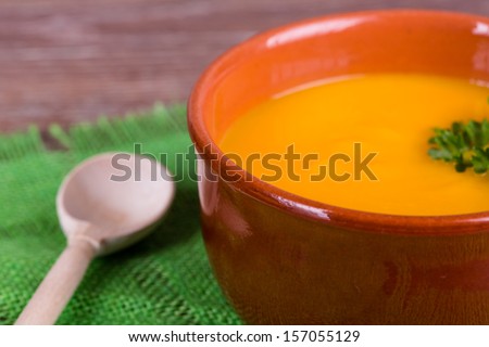 Bowl of pumpkin soup with parsley on wooden background