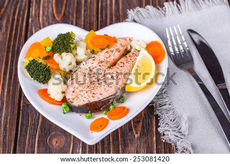 Steamed salmon with vegetables on  plate in the form of heart on wooden background