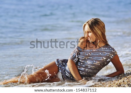 the young fashionable woman lies on the sandy coast in water in wet clothes