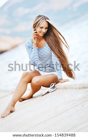 Beautiful sexy woman wearing sailor striped shirt  posing at the sea on a wooden pier