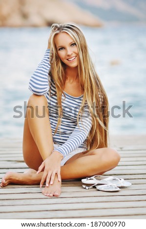 Beautiful sexy woman wearing sailor striped shirt posing at the sea on a wooden pier