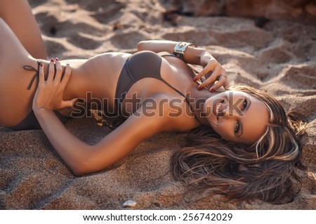 Sexy woman in a swimsuit relaxing on the sand of the beach. Tan skin