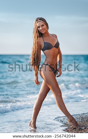 Sexy woman in a swimsuit relaxing on the sand of the beach. Tan skin