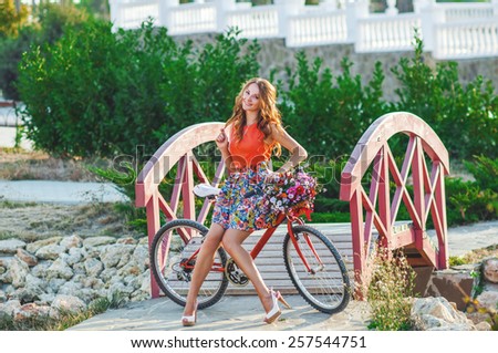 Woman wearing a spring skirt like vintage pin-up holding bicycle with some colorful flowers in the basket in old town