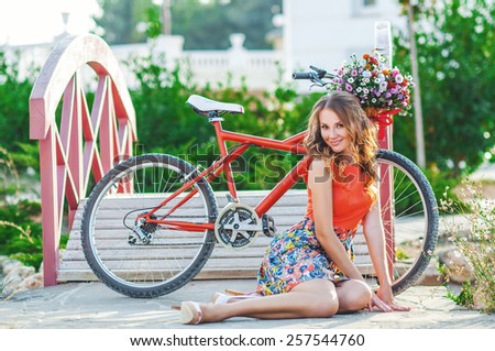 Woman wearing a spring skirt like vintage pin-up holding bicycle with some colorful flowers in the basket in old town