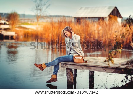 glamourous portrait of the young beautiful woman in leather boots on the bank of a lake on wooden pier