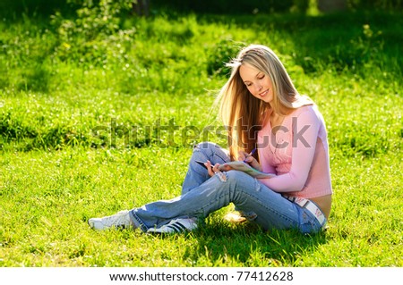 Young beautiful blond girl sitting on the grass and making notes in college lawn