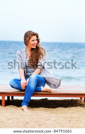 The attractive bright girl sits on the bank of a beach smiles