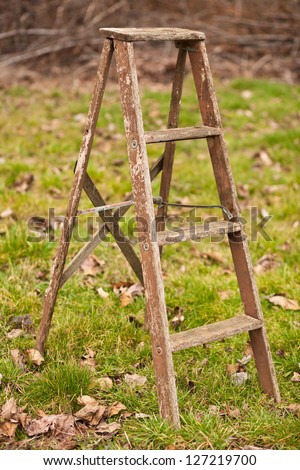 An old, wooden step ladder in a grassy yard.