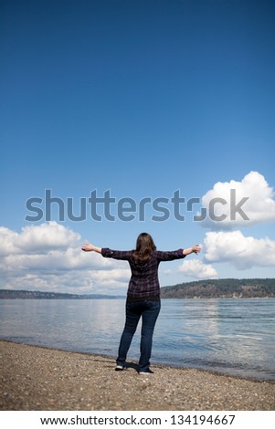 Woman standing in front of the ocean with her arms wide open.