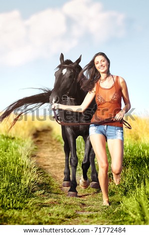 Young beautiful girl walking with a horse on the field