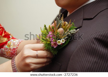 asian bride putting corsage on groom\'s jacket