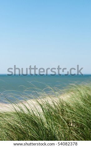 An isolated sand dune in a beach with clear green water and blue sky.