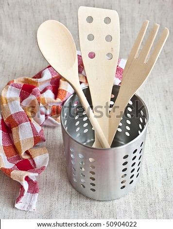 Wooden spoons in a metal jar with kitchen towel on fabric background