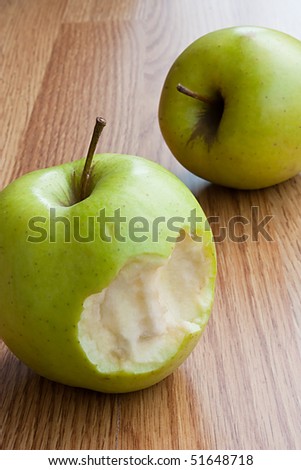Green apples with bite on wooden table