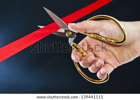 Cutting a red ribbon with scissors on a dark background.