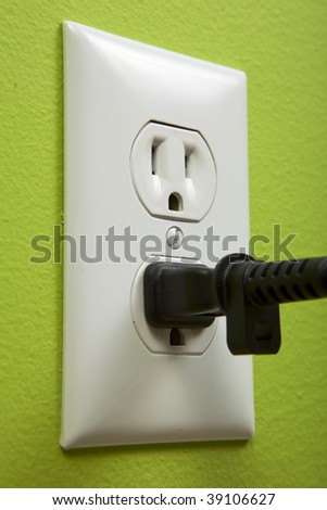 black cable plugged in a white electric outlet mounted on green wall