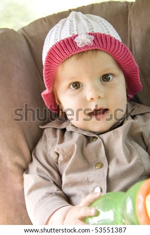 The surprised girl sits with widely open eyes and a mouth in a cap and holds an empty bottle in hands