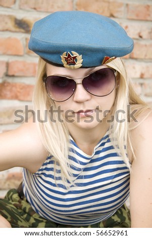 The woman in the military form and sun glasses sits near a brick wall