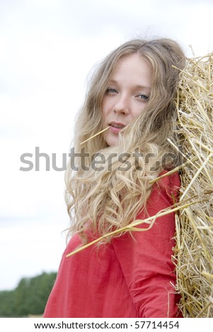 The woman in a red dress costs near a stack of straw and holds in a mouth a straw