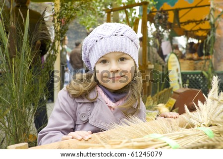 The girl in a violet raincoat and a cap costs near a cart with wheat crop