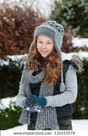 Cheerful teenager girl in winter cloths making a snowball