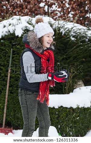 Cheerful teenager girl in winter cloths making a snowball