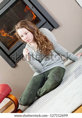 Blond teenager girl sitting on carpet near fireplace