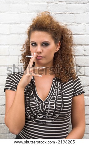 Smoking brunette girl standing next to a brick wall
