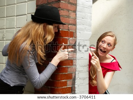 Two girls peeking around the two sides of the wall at house entrance