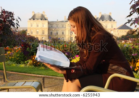 Pretty girl reading magazine in Luxembourg garden (Paris). Late afternoon sun. Autumn colors.