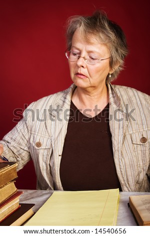 Mature woman with old books takes notes in notepad