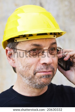Mature man in yellow hard hat speaking on mobile phone