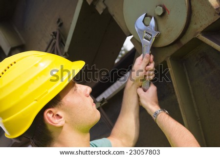 Worker in protective clothes fixing a large machine with an adjustable wrench