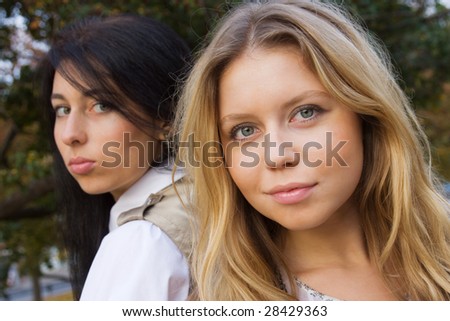 Two girls standing back to back; photographed outdoors