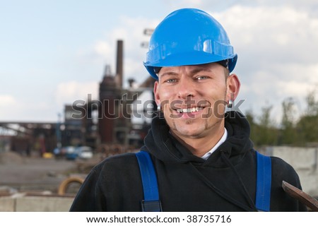 Smiling worker in blue hard hat standing against industrial background