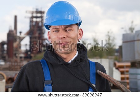Smiling worker in blue hard hat standing against industrial background