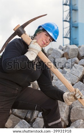 Female blue collar worker in protective clothes holding pickaxe