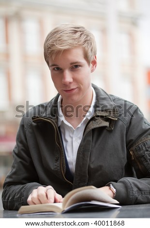 Young blond handsome smiling guy sitting with a book