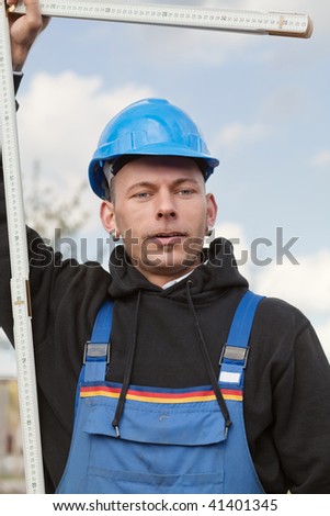 Manual worker in hard hat stands outdoor with foldable ruler