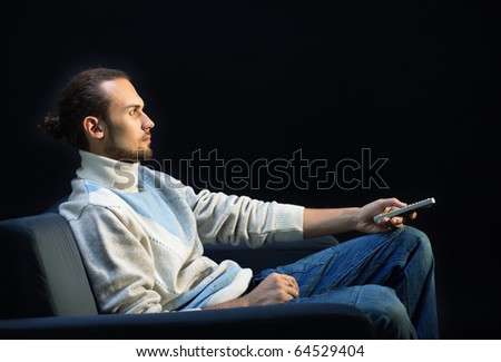 Handsome man sitting on the couch in the dark changing TV channeels with remote control