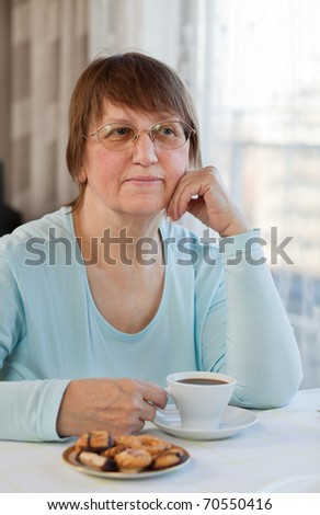 Elderly woman enjoying a cup of coffee with cookies at home