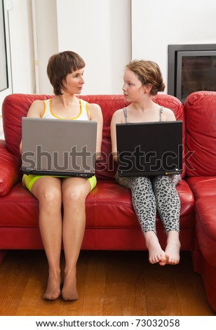 Mom and her daughter sitting on red sofa with their laptops