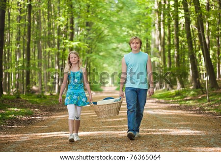 Teenager brother and sister walking along the path in the woods, carrying picnic basket