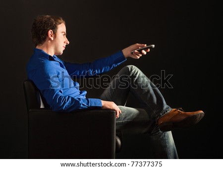 Handsome man sitting on the armchair in the dark changing TV channels with remote control
