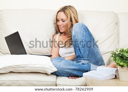 Pretty smiling young woman sitting on white couch with laptop computer