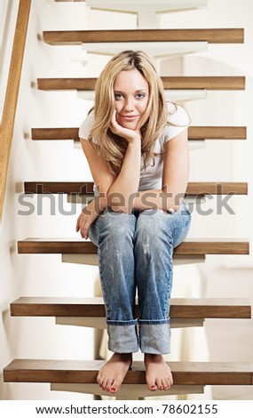 Pretty young smiling woman sitting on steps at home