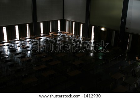 Examination hall at a university, with the lights out waiting for the exams to start.  Desks and chairs silhouetted against the windows.