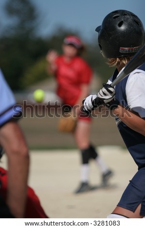 Left handed woman softball player watches as the ball comes towards her, ready for the big hit, shallow DOF means ball, pitcher & background is out of focus.